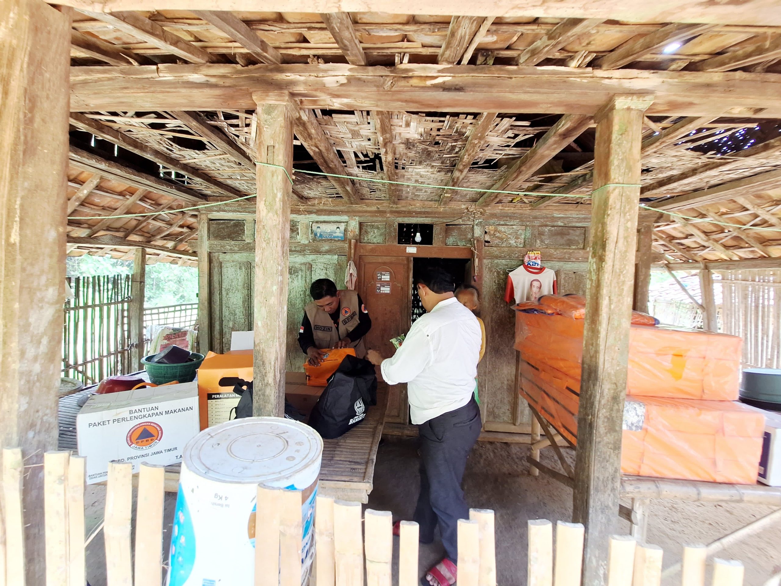 Petugas BPBD Kabupaten Sampang menyalurkan bantuan logistik kepada dua lansia yang tinggal di gubuk tak layak huni di Dusun Lenteng, Desa Nyeloh, Kecamatan Kedungdung, Selasa (13/1/2026). Bantuan diberikan sebagai bentuk kepedulian kemanusiaan untuk menopang kebutuhan dasar dan kondisi kesehatan lansia rentan.