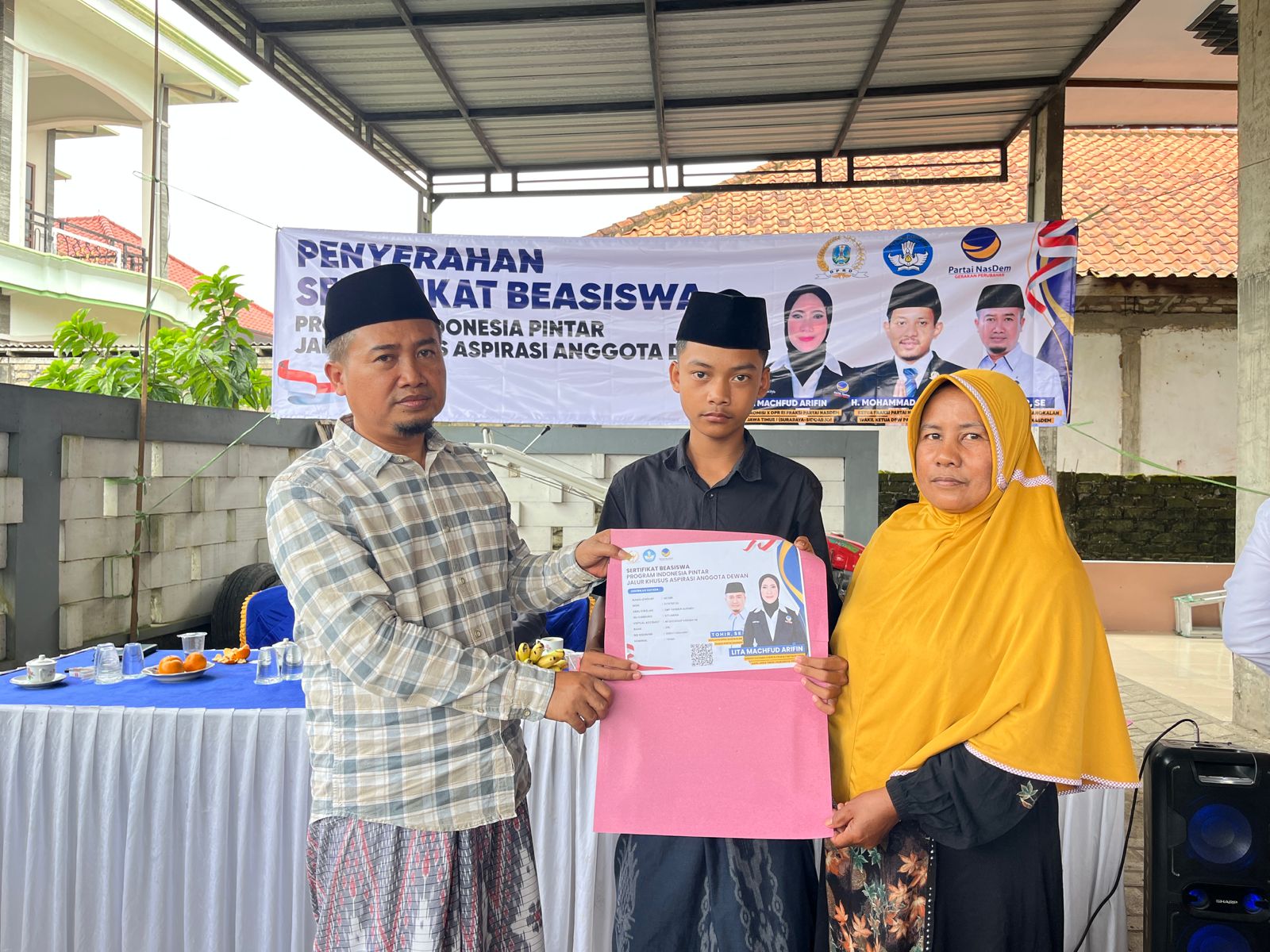 Seorang siswa didampingi orang tua menerima sertifikat bantuan Program Indonesia Pintar (PIP) jalur aspirasi anggota DPRD Kabupaten Bangkalan dari Partai NasDem dalam kegiatan penyerahan bantuan pendidikan di Dusun Naro’an, Kelurahan Tunjung, Kecamatan Burneh, Jumat (16/01/2026).