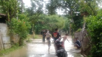 Warga melintasi jalan desa yang terendam banjir akibat hujan deras di Kabupaten Sampang, Madura, Minggu (4/1/2026). BPBD Sampang menetapkan status Siaga II dan mengimbau masyarakat waspada terhadap potensi banjir susulan.