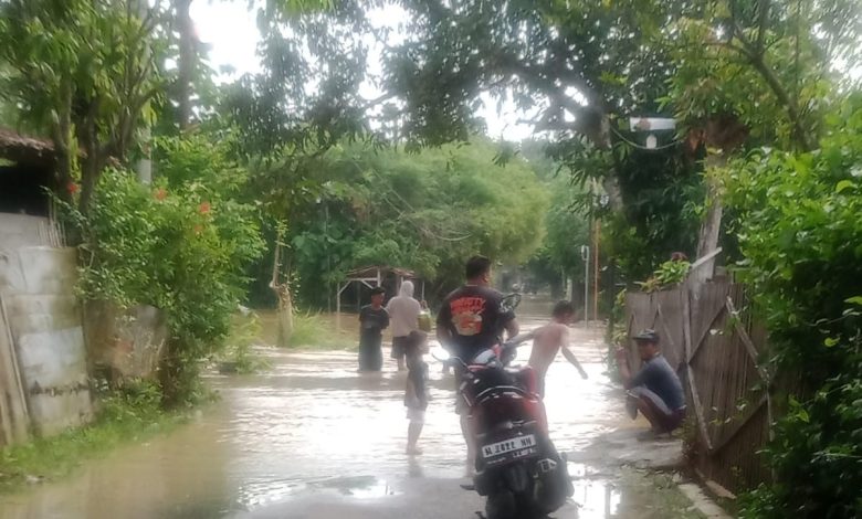 Warga melintasi jalan desa yang terendam banjir akibat hujan deras di Kabupaten Sampang, Madura, Minggu (4/1/2026). BPBD Sampang menetapkan status Siaga II dan mengimbau masyarakat waspada terhadap potensi banjir susulan.