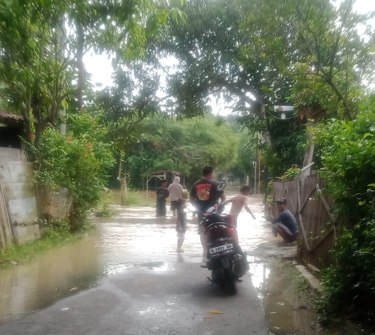 Warga melintasi jalan desa yang terendam banjir akibat hujan deras di Kabupaten Sampang, Madura, Minggu (4/1/2026). BPBD Sampang menetapkan status Siaga II dan mengimbau masyarakat waspada terhadap potensi banjir susulan.