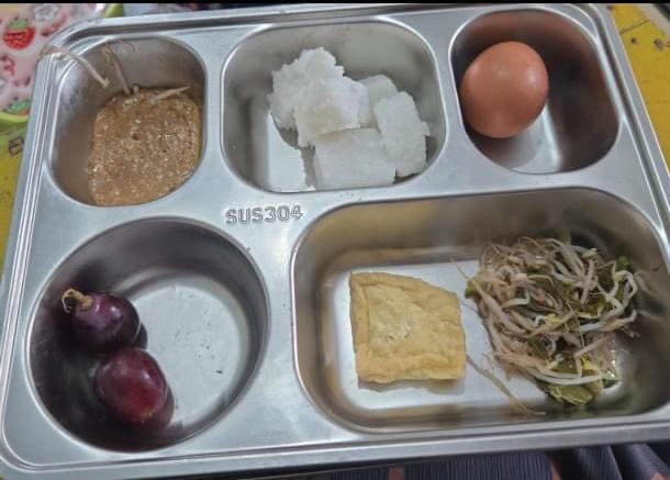 Menu Makan Bergizi Gratis (MBG) yang diterima siswa SDN Poter 1 Tanah Merah, terdiri dari lontong, telur rebus, tahu goreng, kecambah, saus kacang, dan dua butir anggur.