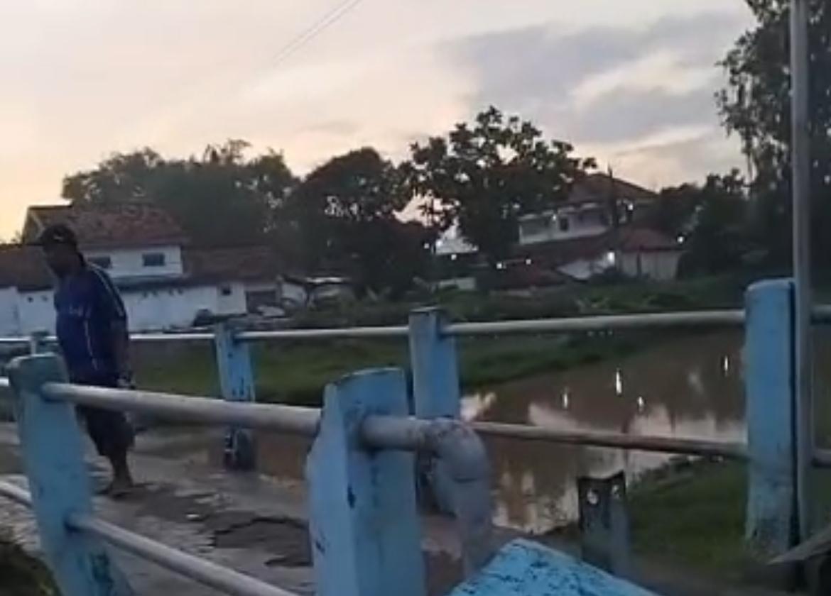 Seorang warga berdiri di atas jembatan di kawasan Sungai Tunjung, Bangkalan, memantau lokasi pencarian bocah 8 tahun yang diduga tenggelam bersama ibunya.