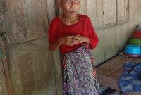 Muslimah (61), perempuan tunanetra di Dusun Kebun, Desa Baturasang, Sampang, berdiri di depan rumah sederhana tempat ia menjalani hidup seorang diri dengan mengandalkan bantuan dari tetangga sekitar.