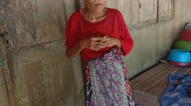 Muslimah (61), perempuan tunanetra di Dusun Kebun, Desa Baturasang, Sampang, berdiri di depan rumah sederhana tempat ia menjalani hidup seorang diri dengan mengandalkan bantuan dari tetangga sekitar.