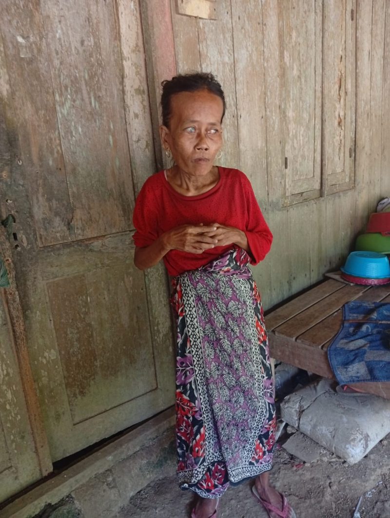 Muslimah (61), perempuan tunanetra di Dusun Kebun, Desa Baturasang, Sampang, berdiri di depan rumah sederhana tempat ia menjalani hidup seorang diri dengan mengandalkan bantuan dari tetangga sekitar.