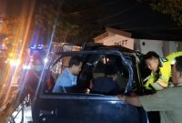 Petugas kepolisian dibantu warga mengevakuasi korban dari mobil pikap yang ringsek parah usai menabrak truk tronton di Jalan Halim Perdana Kusuma, Bancaran, Bangkalan, Minggu malam (5/4/2026). Satu orang meninggal dunia, sementara empat lainnya mengalami luka-luka.