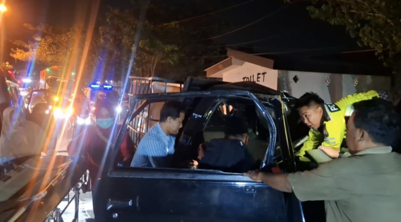 Petugas kepolisian dibantu warga mengevakuasi korban dari mobil pikap yang ringsek parah usai menabrak truk tronton di Jalan Halim Perdana Kusuma, Bancaran, Bangkalan, Minggu malam (5/4/2026). Satu orang meninggal dunia, sementara empat lainnya mengalami luka-luka.