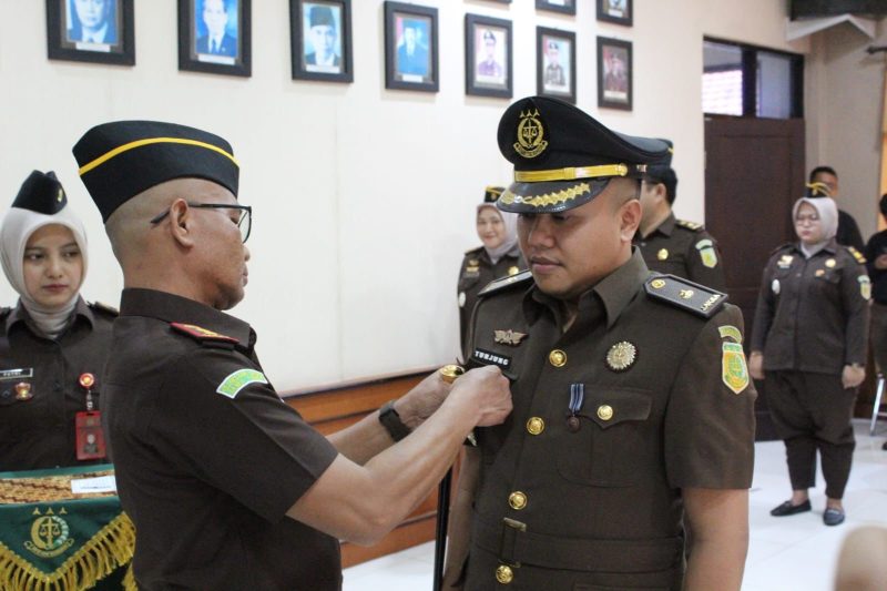Kajari Sampang Mochamad Iqbal menyematkan tanda jabatan kepada Tunjung Sughandiko saat prosesi pelantikan dan serah terima jabatan Kasi Pidum di Kejaksaan Negeri Sampang, Jumat (24/4/2026).